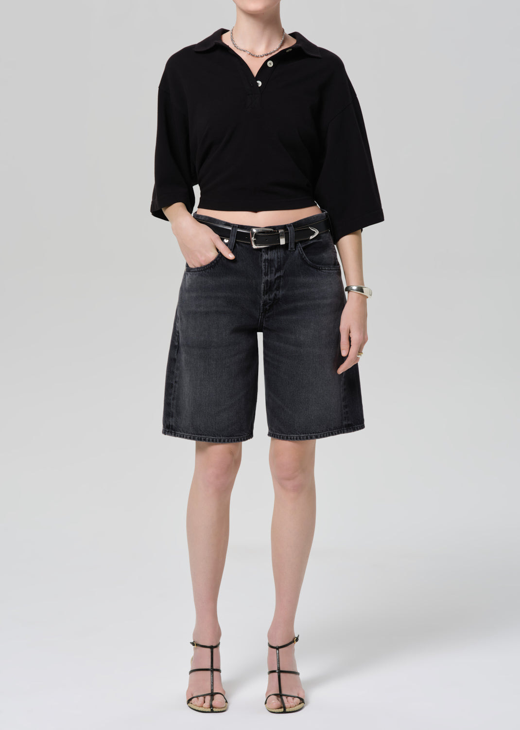 Person wearing a black cropped polo and black denim shorts on a gray background