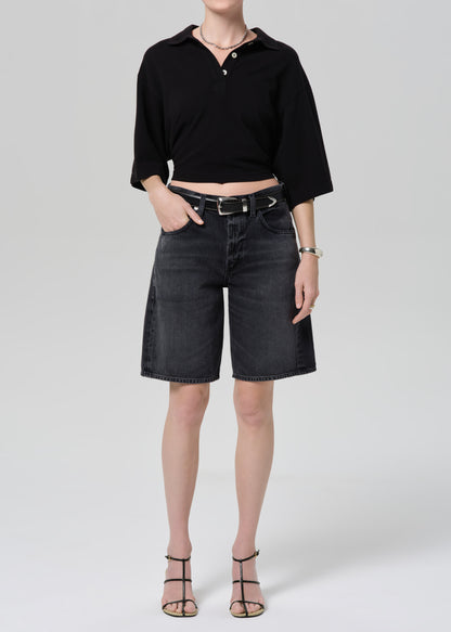 Person wearing a black cropped polo and black denim shorts on a gray background