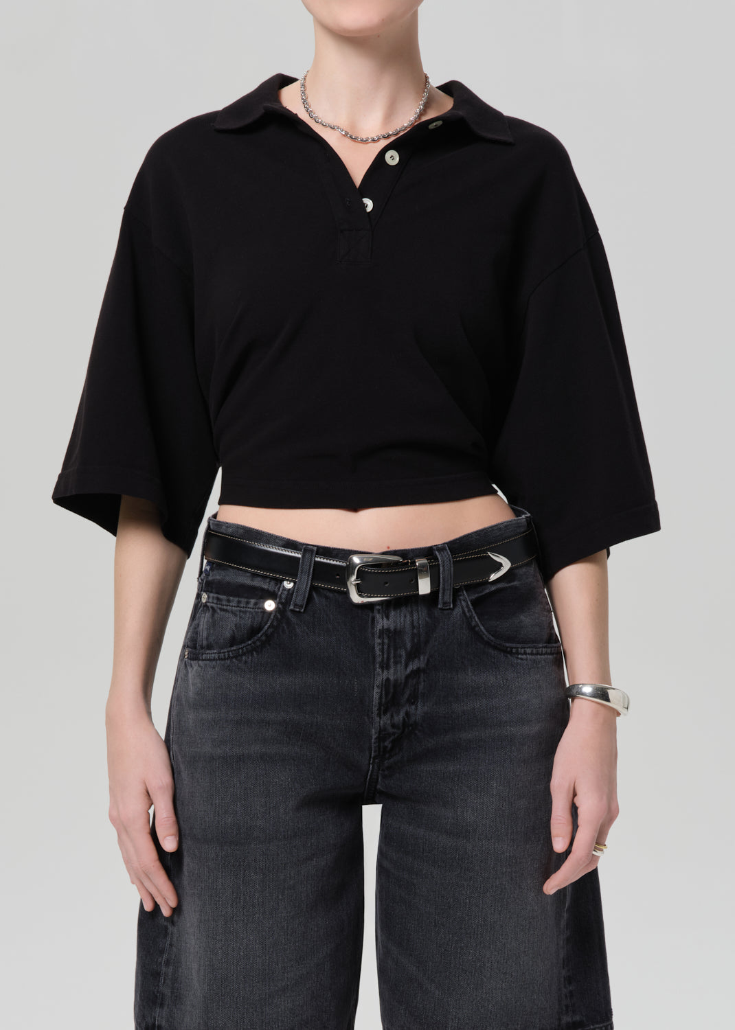 Person wearing a black cropped polo and black denim shorts on a gray background