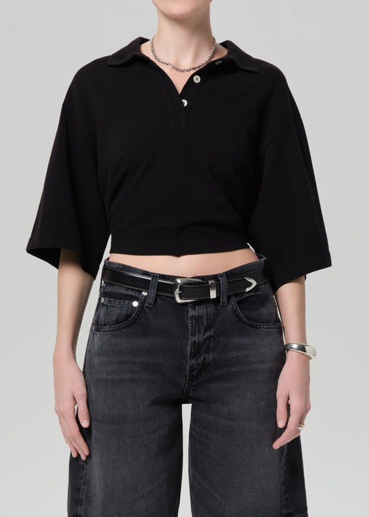 Person wearing a black cropped polo and black denim shorts on a gray background