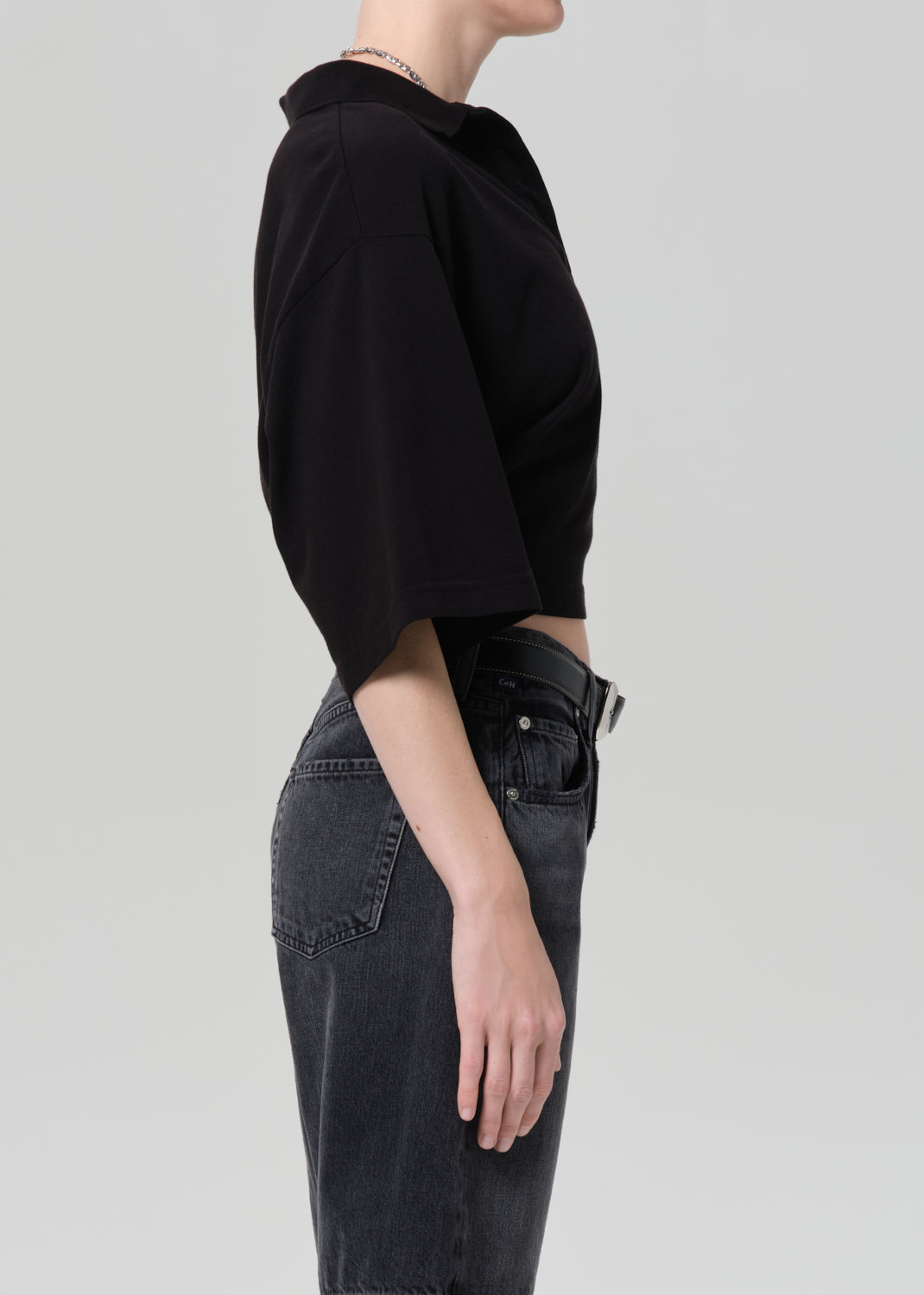 Person wearing a black cropped polo and black denim shorts on a gray background
