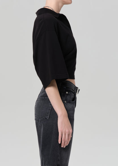 Person wearing a black cropped polo and black denim shorts on a gray background