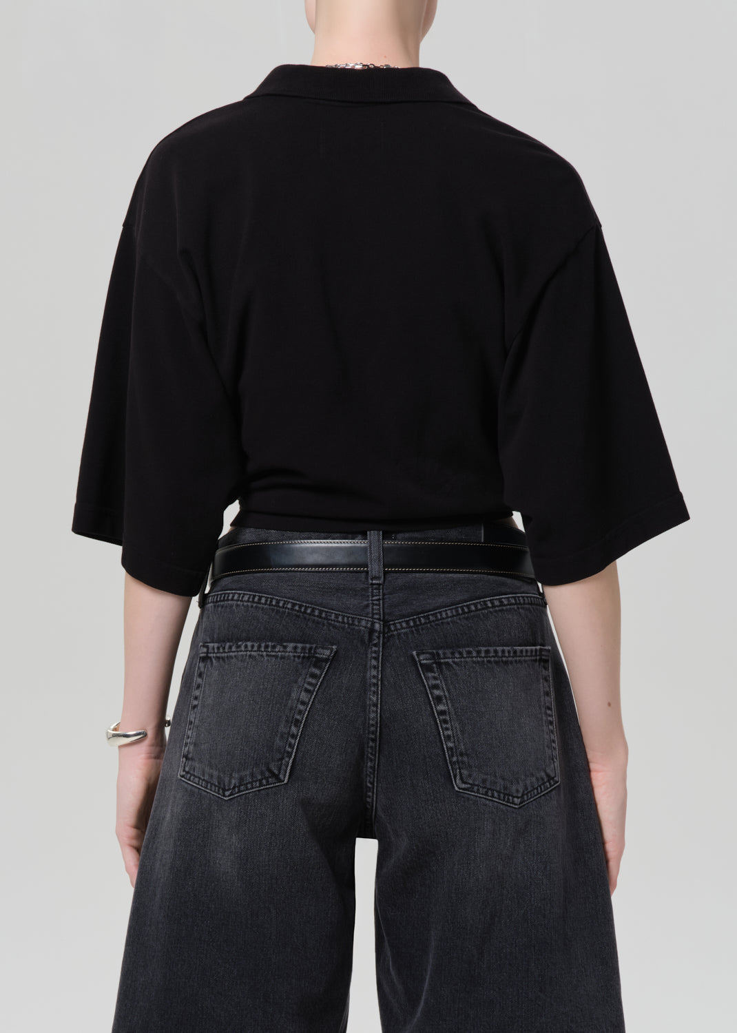 Person wearing a black cropped polo and black denim shorts on a gray background