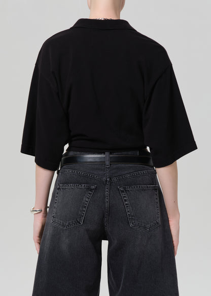 Person wearing a black cropped polo and black denim shorts on a gray background