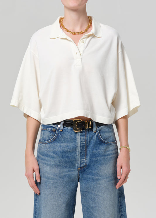 Person wearing a white shirt and blue jeans with a gold necklace on a gray background