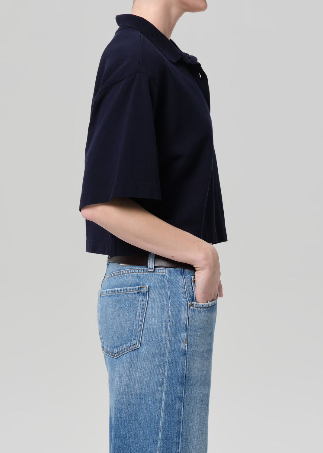 Person wearing a navy blue top and blue jeans on a light gray background
