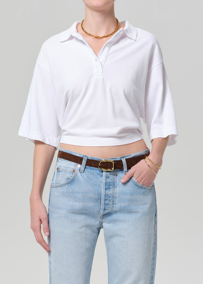 Person wearing a white cropped shirt and light blue jeans with a brown belt on a gray background