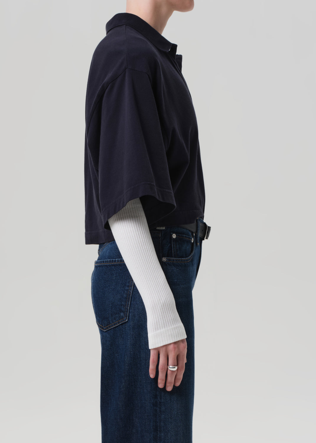 Person wearing navy polo, white long-sleeve shirt, and blue jeans on a light gray background