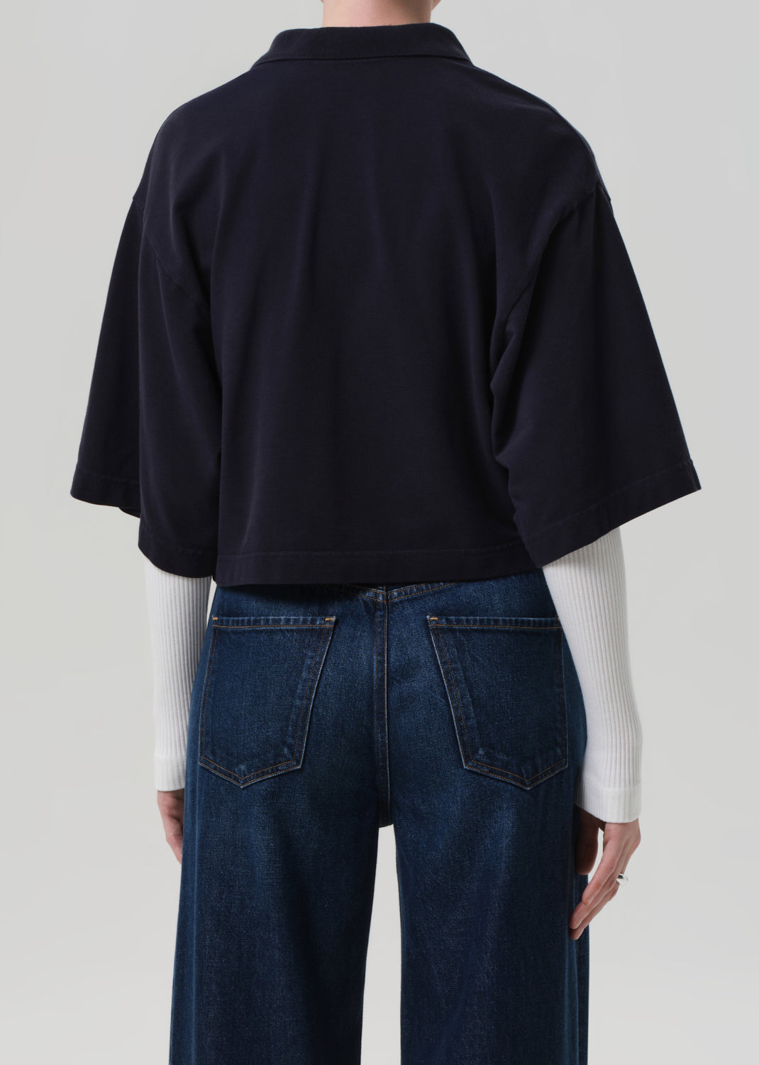Person wearing a navy oversized shirt and blue jeans on a plain background