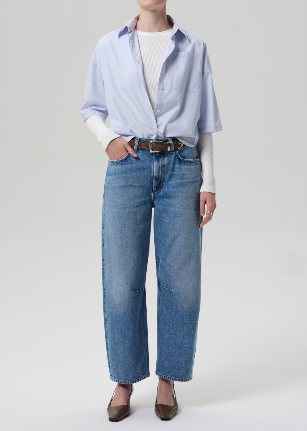 Person wearing a light blue shirt, white sweater, and blue jeans on a plain background