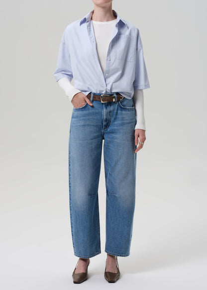 Person wearing a light blue shirt, white sweater, and blue jeans on a plain background