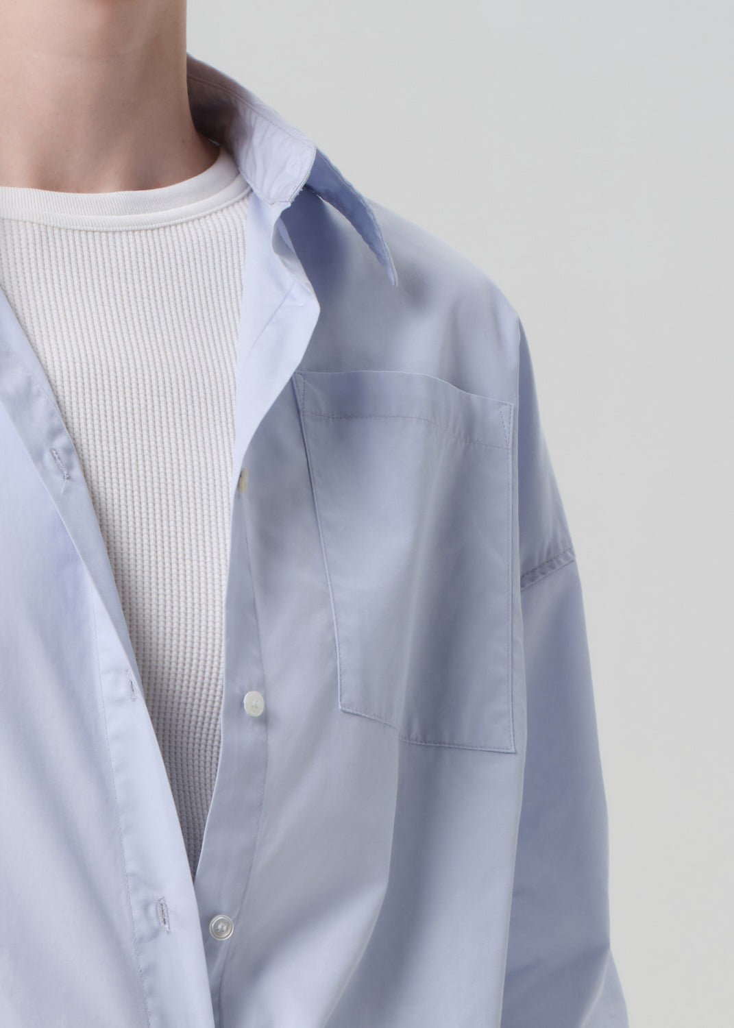 Light blue shirt over a white ribbed sweater on a plain background