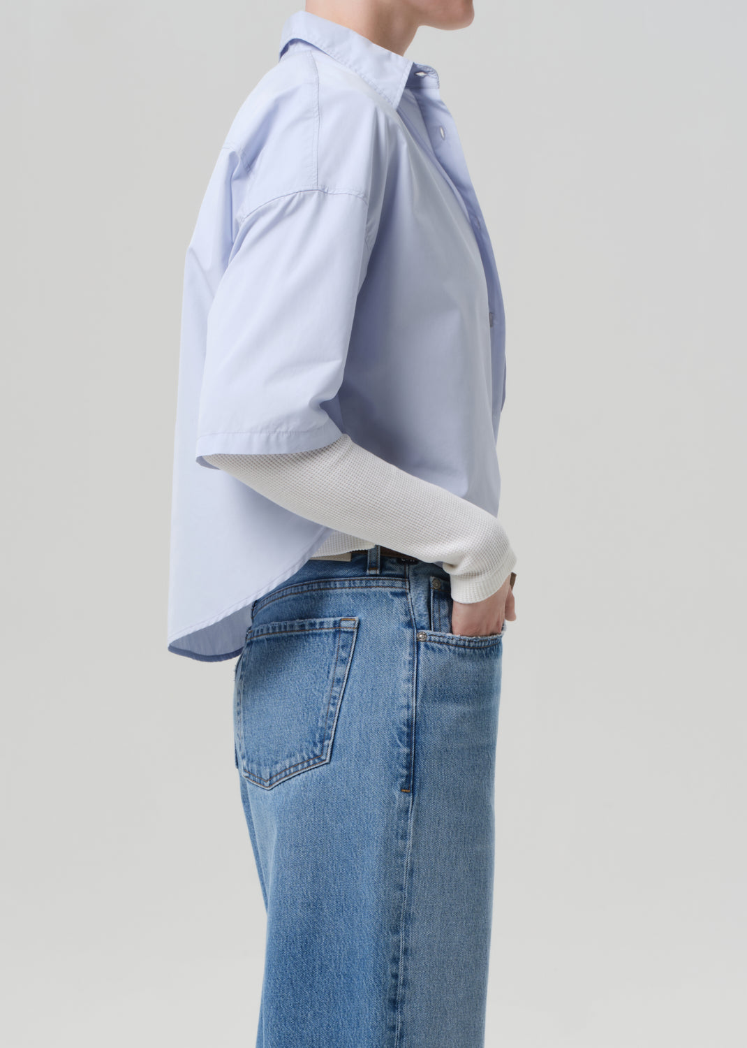 Person wearing a light blue button-up shirt and jeans on a plain background