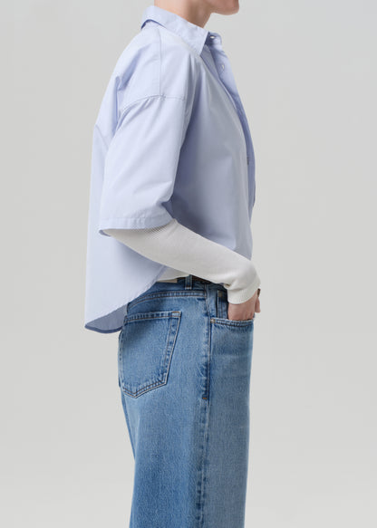 Person wearing a light blue button-up shirt and jeans on a plain background