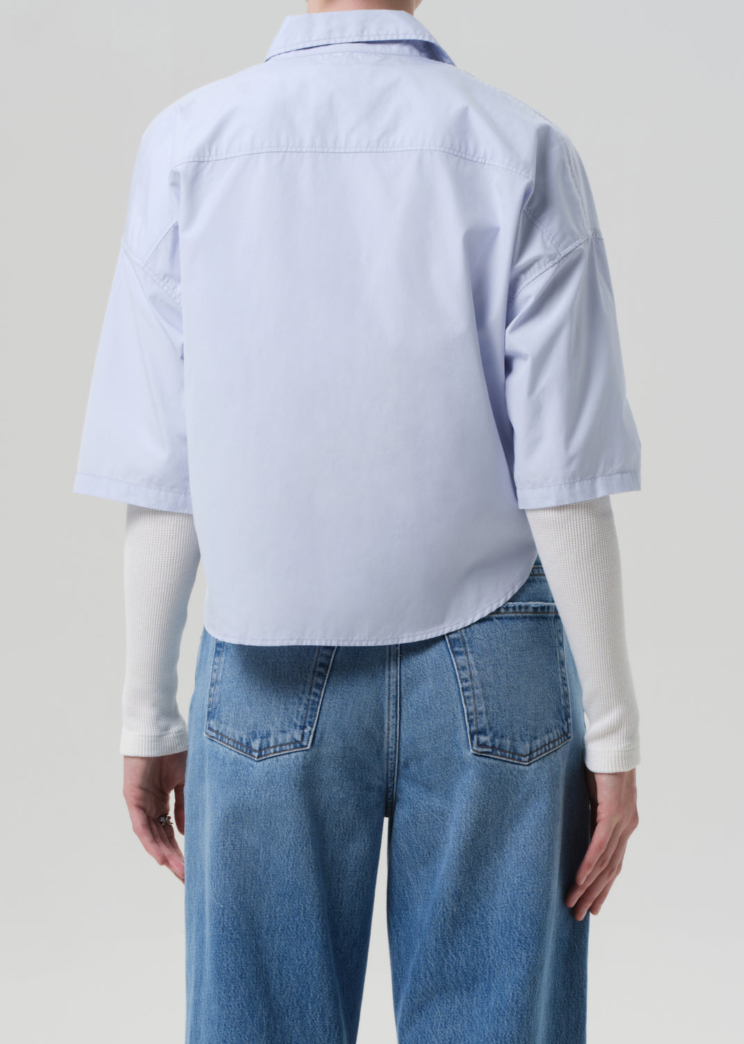 Person wearing a light blue shirt and jeans on a plain background