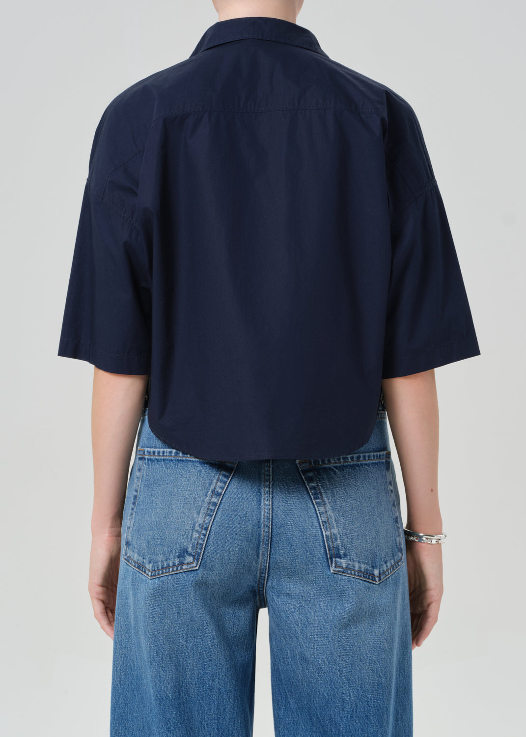 Person wearing a navy blue shirt and blue jeans on a plain background