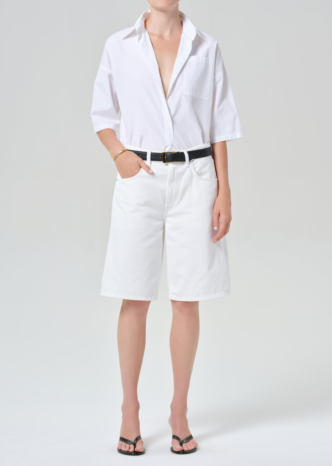 Person wearing a white button-up shirt and white shorts on a plain background