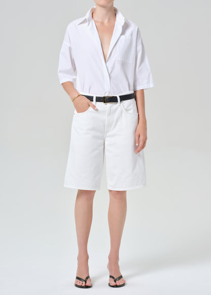 Person wearing a white button-up shirt and white shorts on a plain background