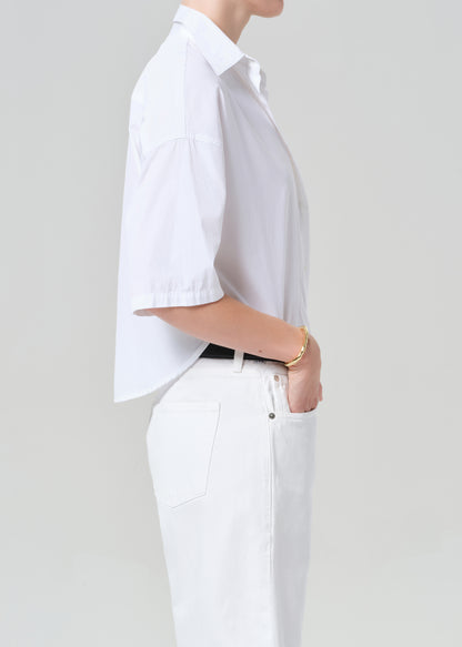 Person wearing a white button-up shirt and white shorts on a plain background