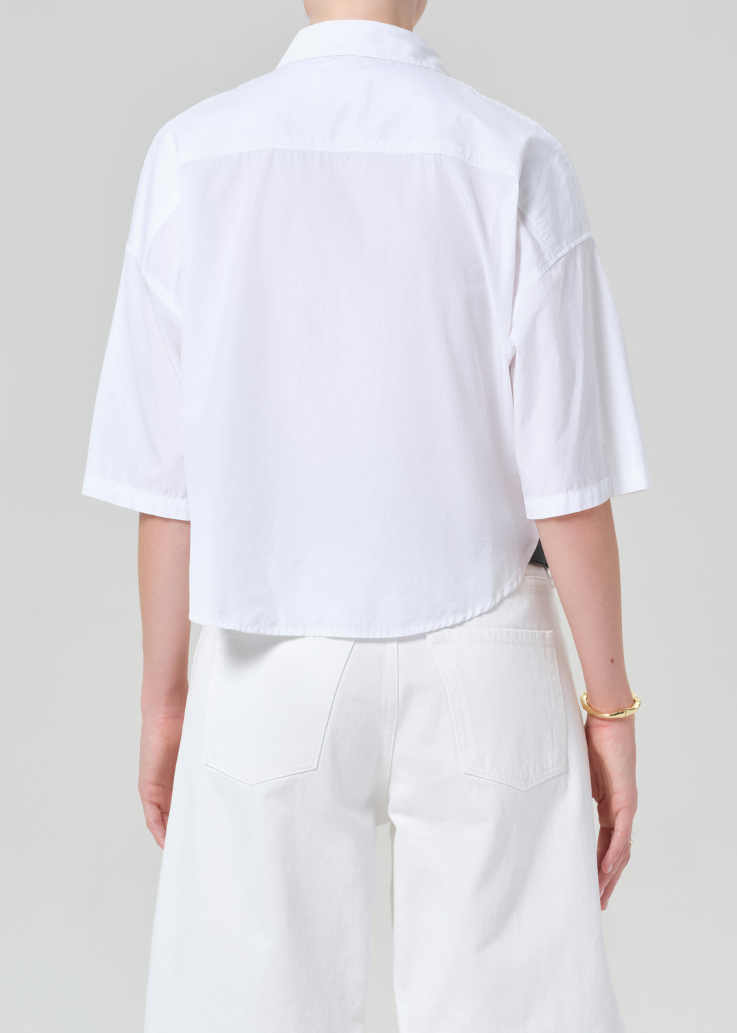 Person wearing a white button-up shirt and white shorts on a plain background