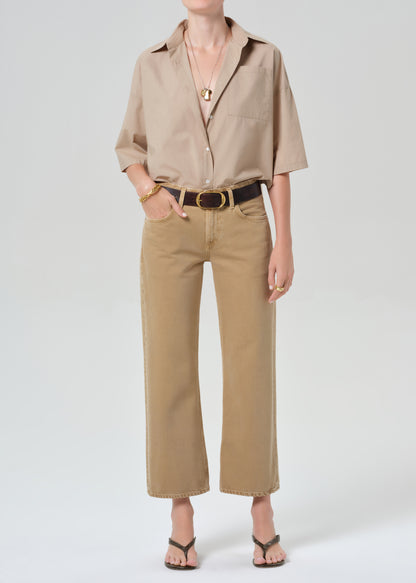 Person wearing a beige shirt and pants with a belt on a grey background