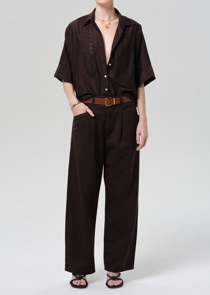 Person wearing a brown shirt and wide-leg pants on a grey background