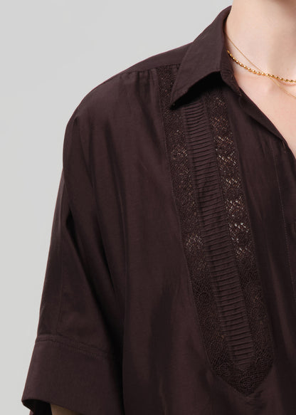 Person wearing a brown button-front shirt with lace inset on a light gray background