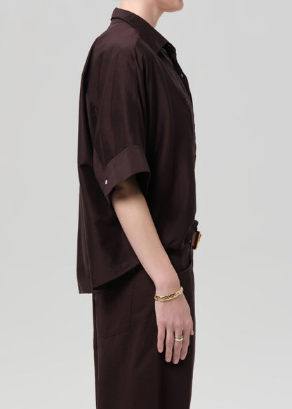 Person wearing a brown shirt and pant set on a light gray background