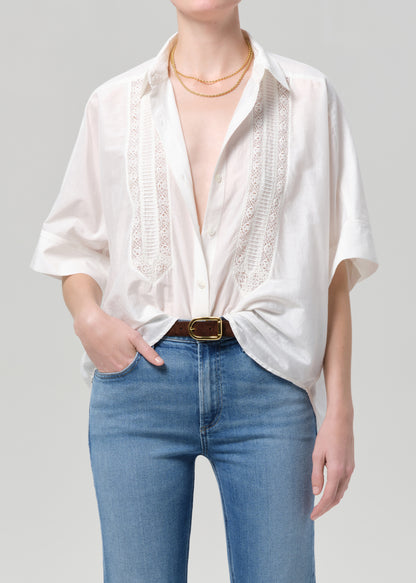 Person wearing a white blouse with lace details and blue jeans on a gray background