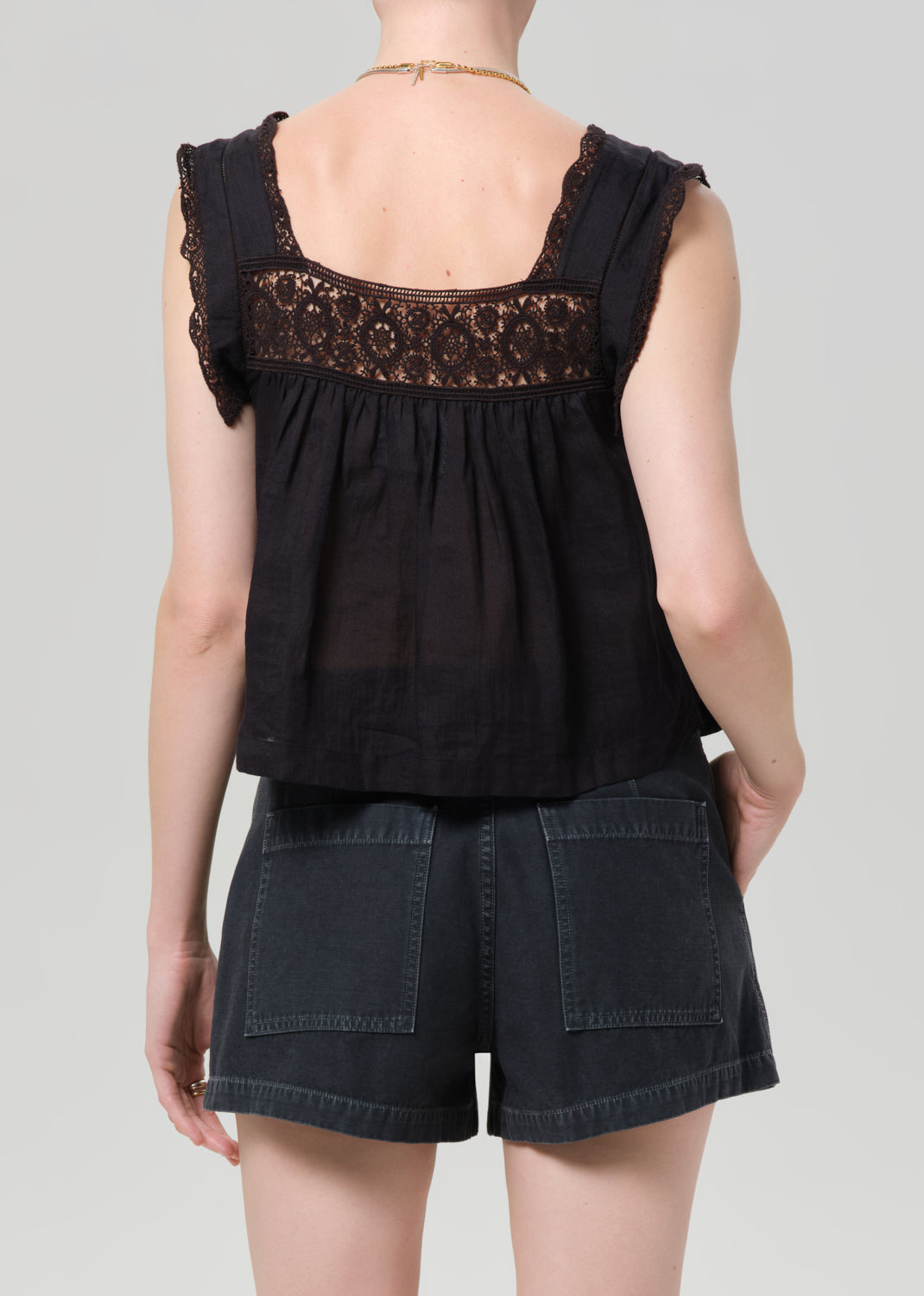 Person wearing a black sleeveless top with lace details and denim shorts on a grey background
