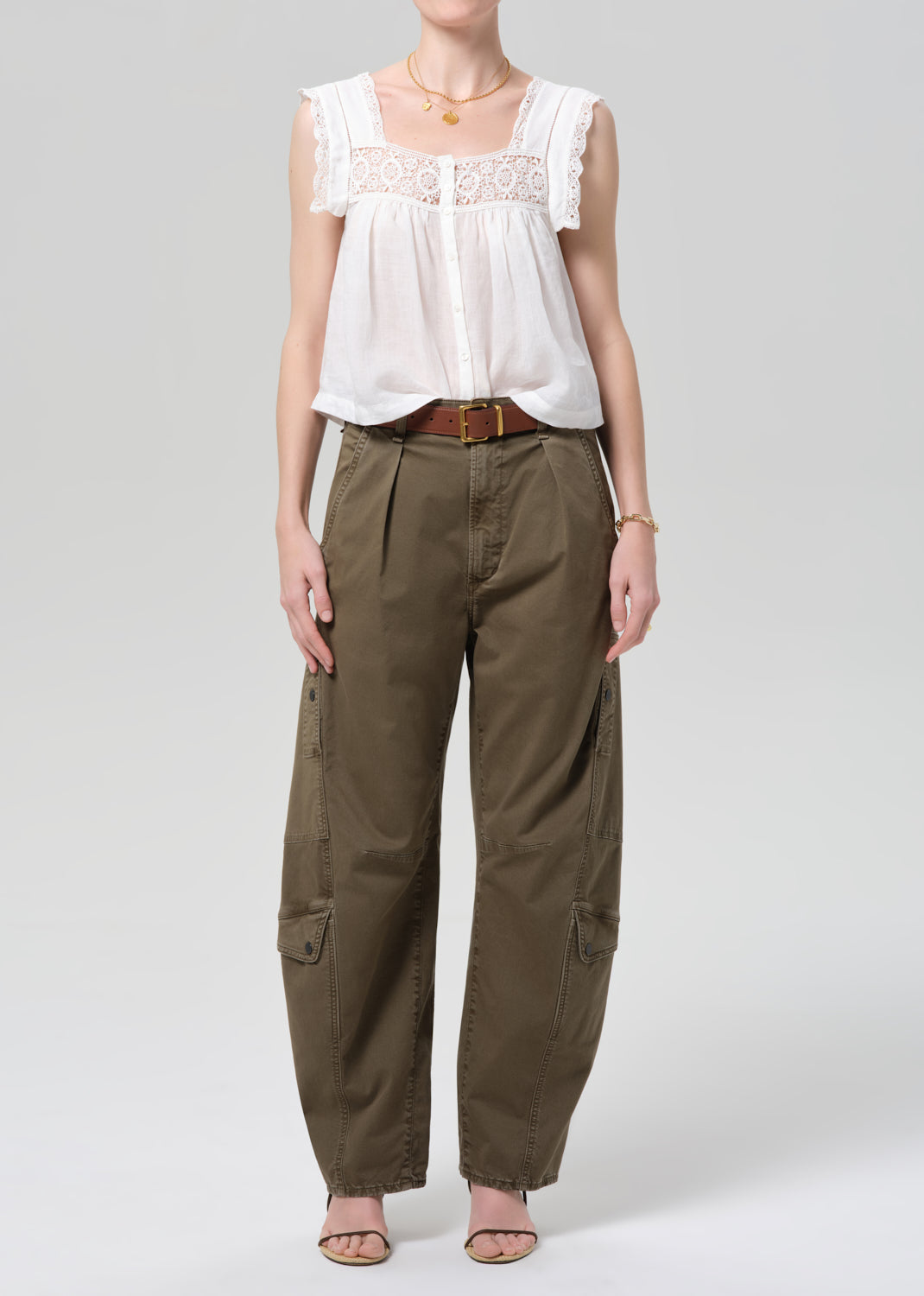 Person wearing a white lace top and olive pants on a gray background
