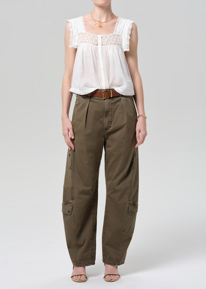 Person wearing a white lace top and olive pants on a gray background