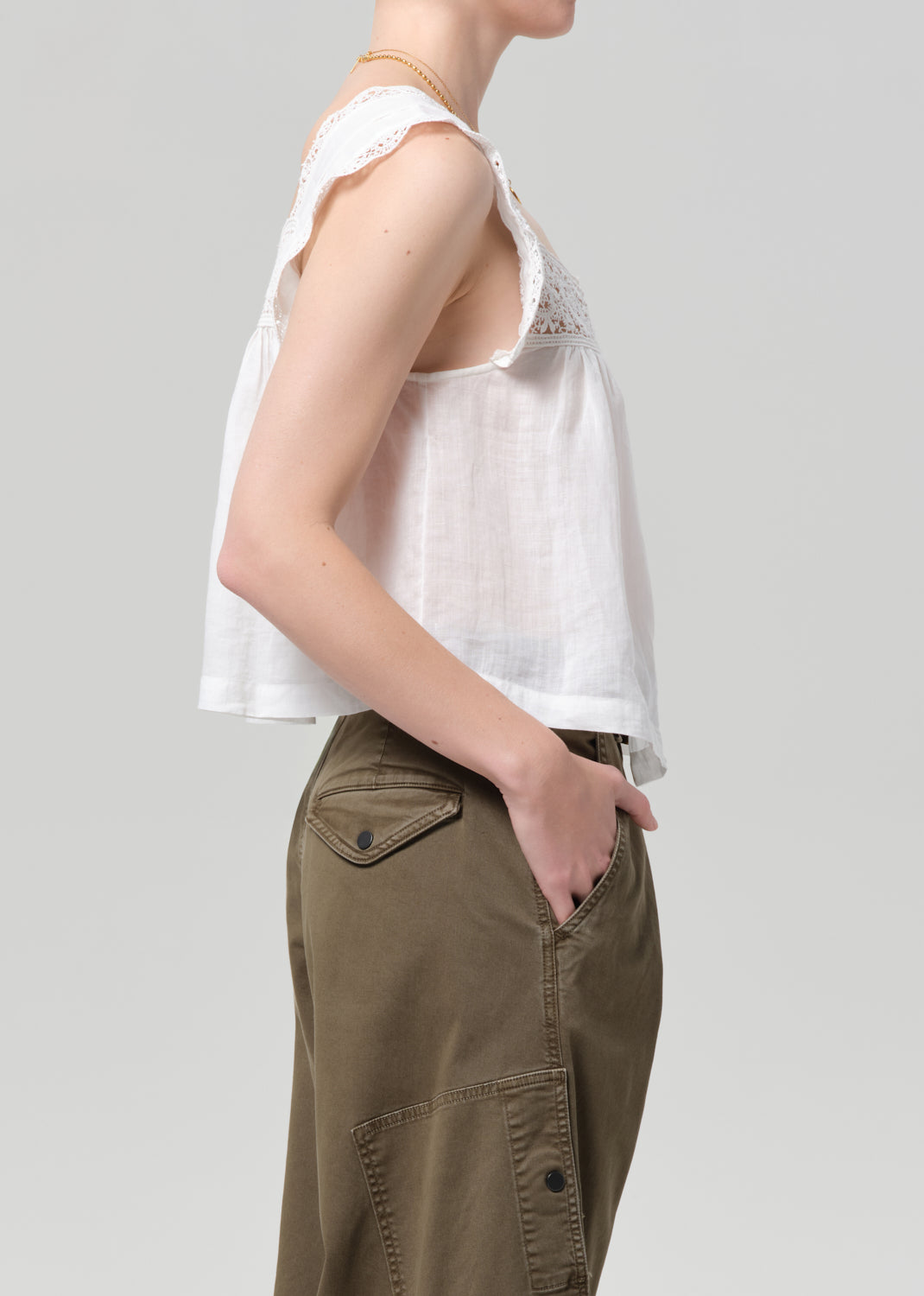 Person wearing a white lace top and olive pants on a gray background