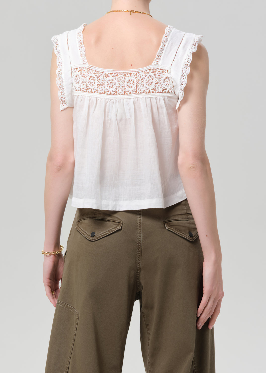 Person wearing a white lace top and olive pants on a gray background