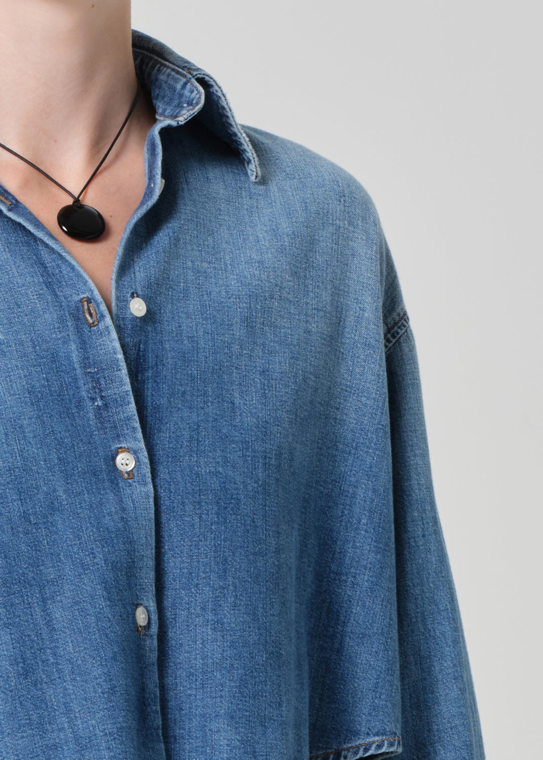 Person wearing a blue denim shirt and white pants on a light gray background