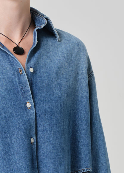 Person wearing a blue denim shirt and white pants on a light gray background