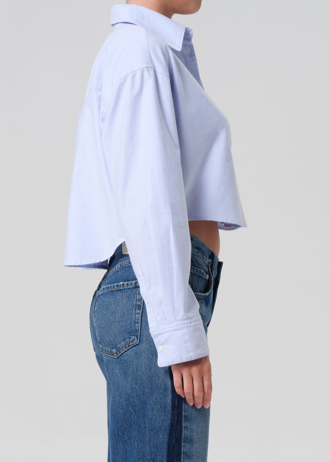 Person wearing a light blue shirt and blue jeans on a plain background