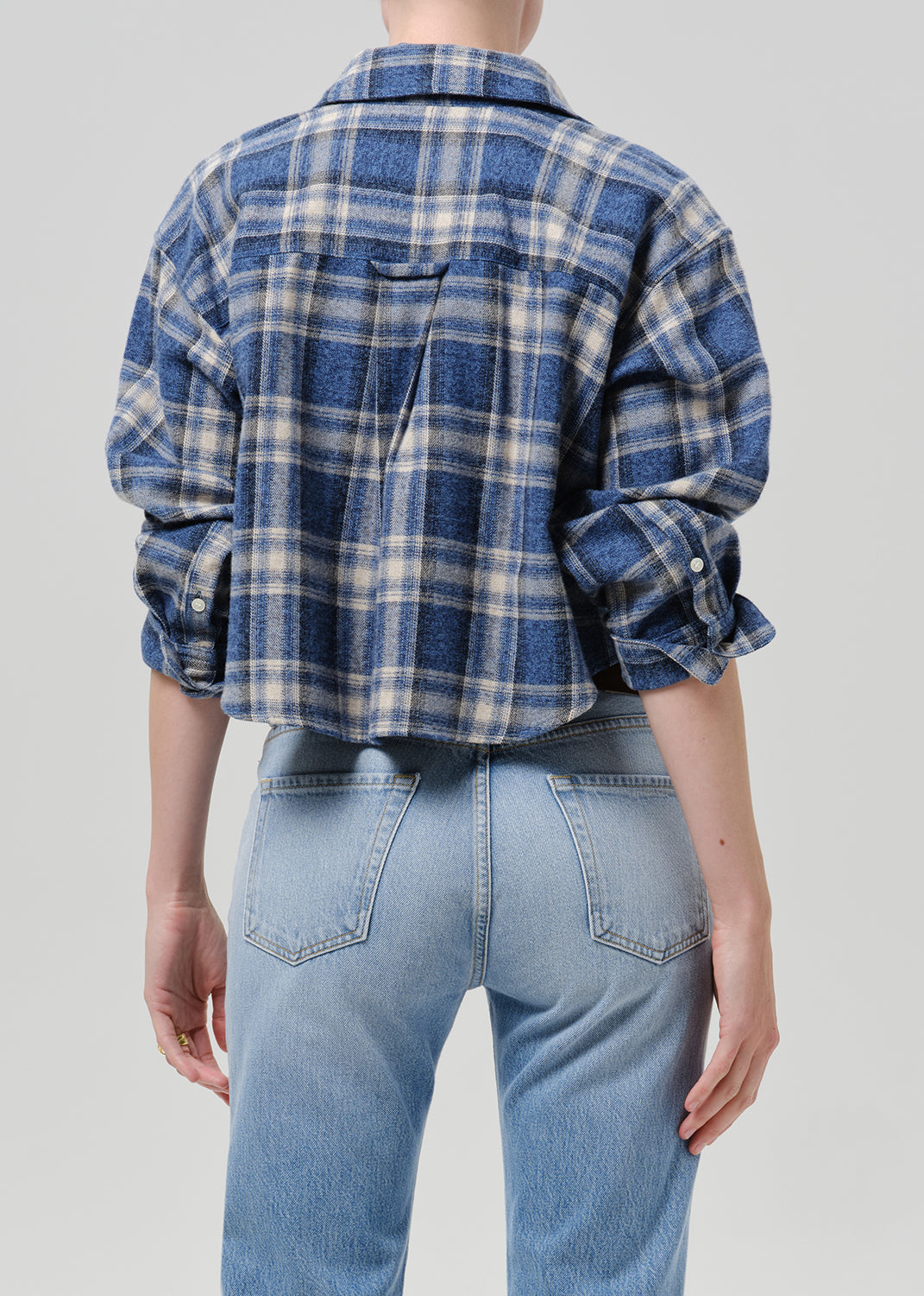 A person shown from the back wearing a cropped blue and white plaid flannel shirt with light-wash jeans, against a grey background.