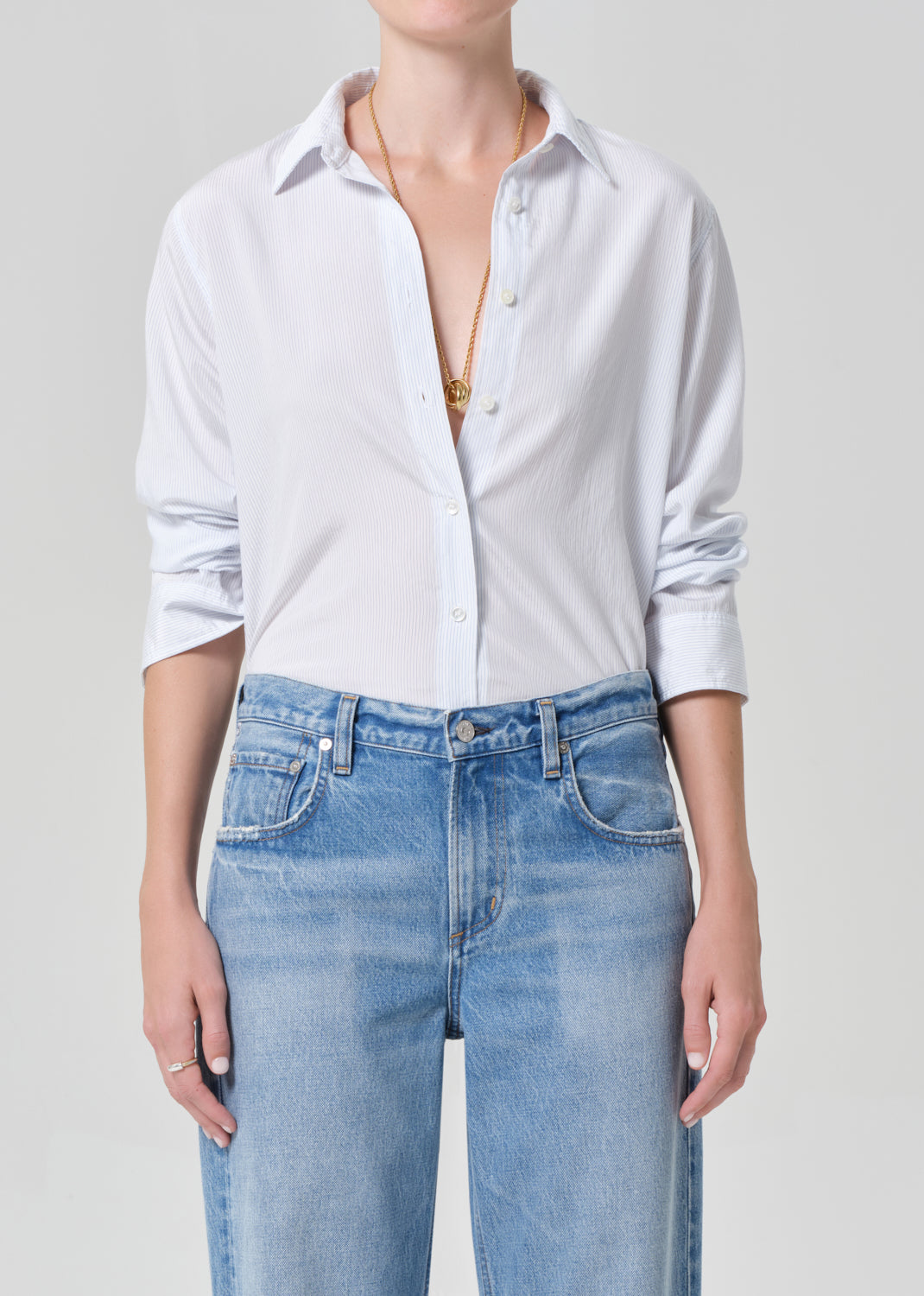 Person wearing a white button-up shirt and blue jeans on a plain background