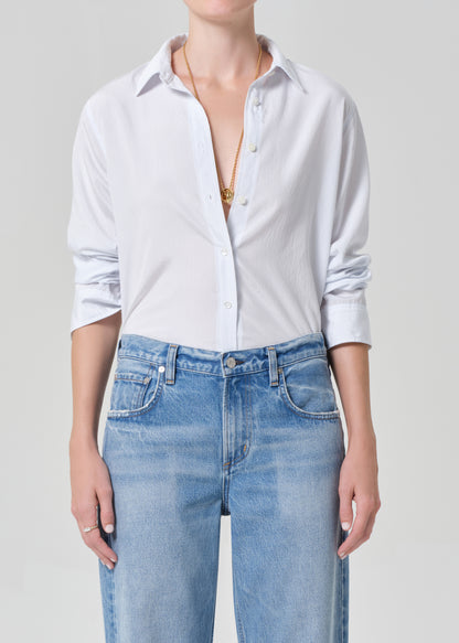 Person wearing a white button-up shirt and blue jeans on a plain background