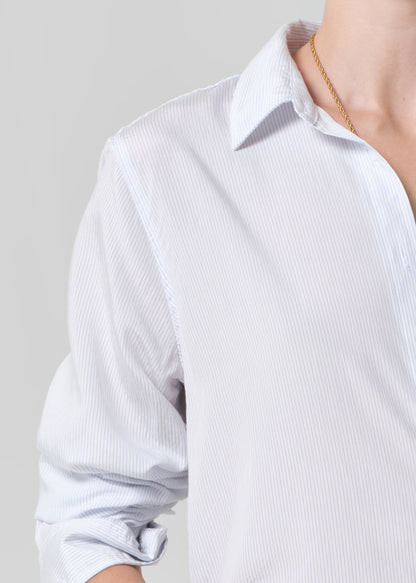 Close-up of a person wearing a light blue striped shirt on a gray background