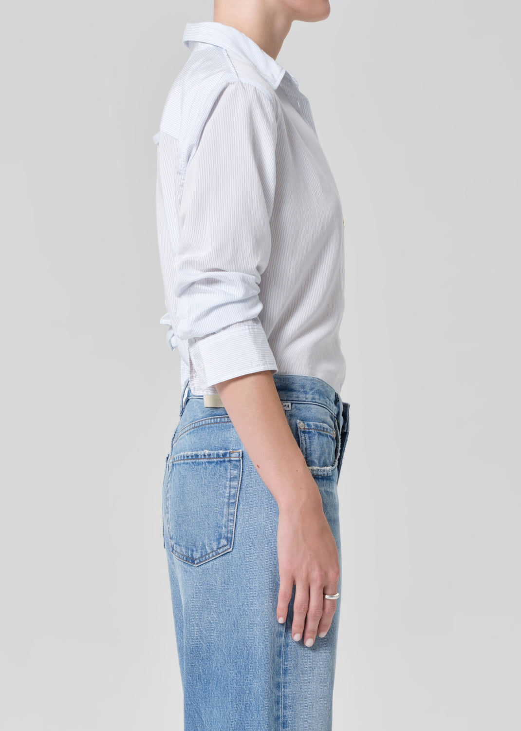 Person wearing a light gray shirt and blue jeans on a plain background