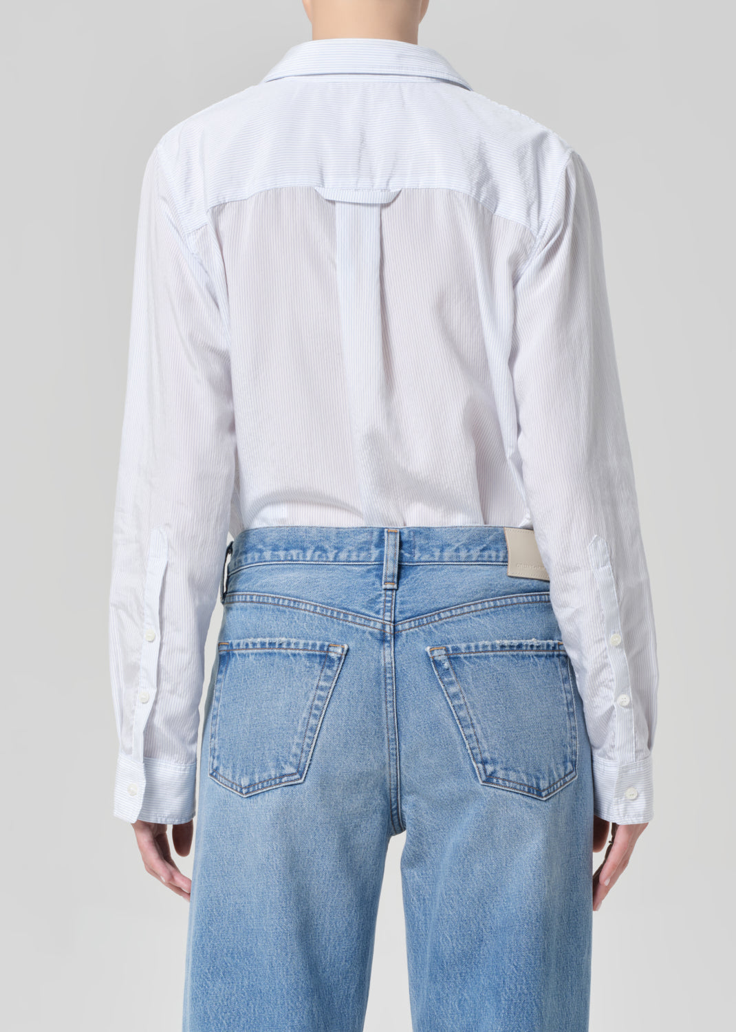 Person wearing a light blue shirt and jeans on a plain background