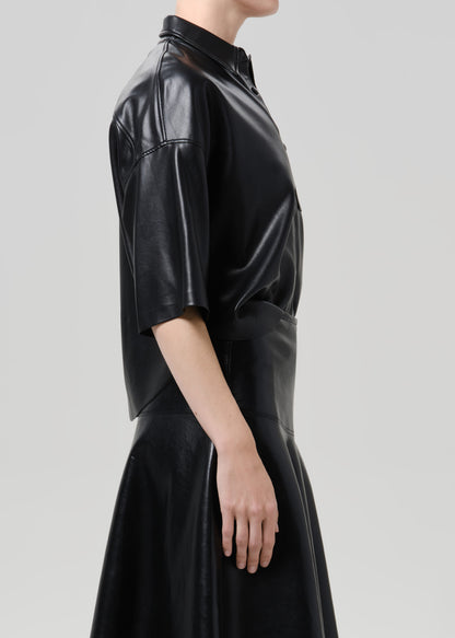 A model shown from the side wearing a black faux-leather midi dress with a collar, short sleeves, and a gathered waist.