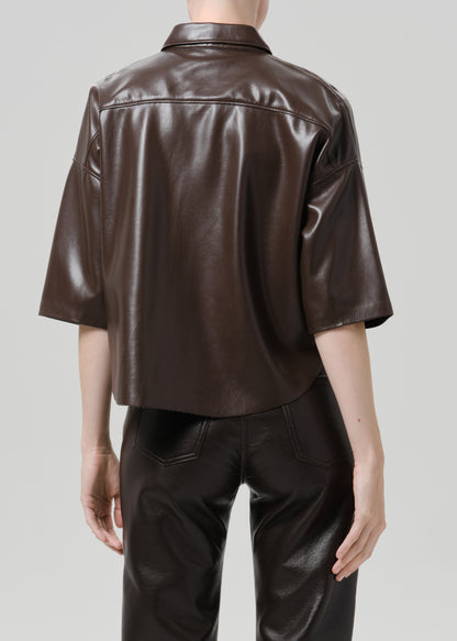A model shown from the back wearing a dark brown cropped leather shirt jacket and matching dark brown leather pants against a grey background.