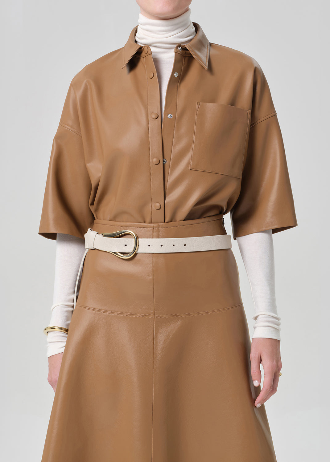 Person wearing a brown leather outfit with a white belt on a gray background