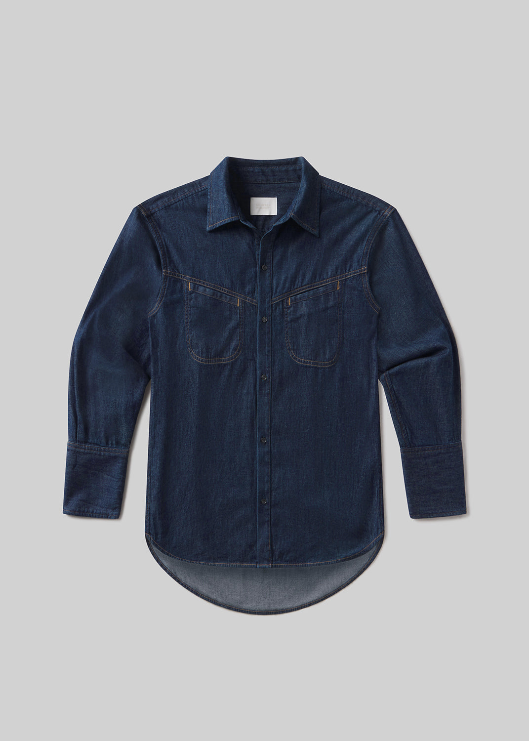 Dark indigo long-sleeve denim shirt with a pointed collar, front button closure, two chest pockets, contrast stitching, buttoned cuffs, and a curved hem, front flat lay view on a grey background