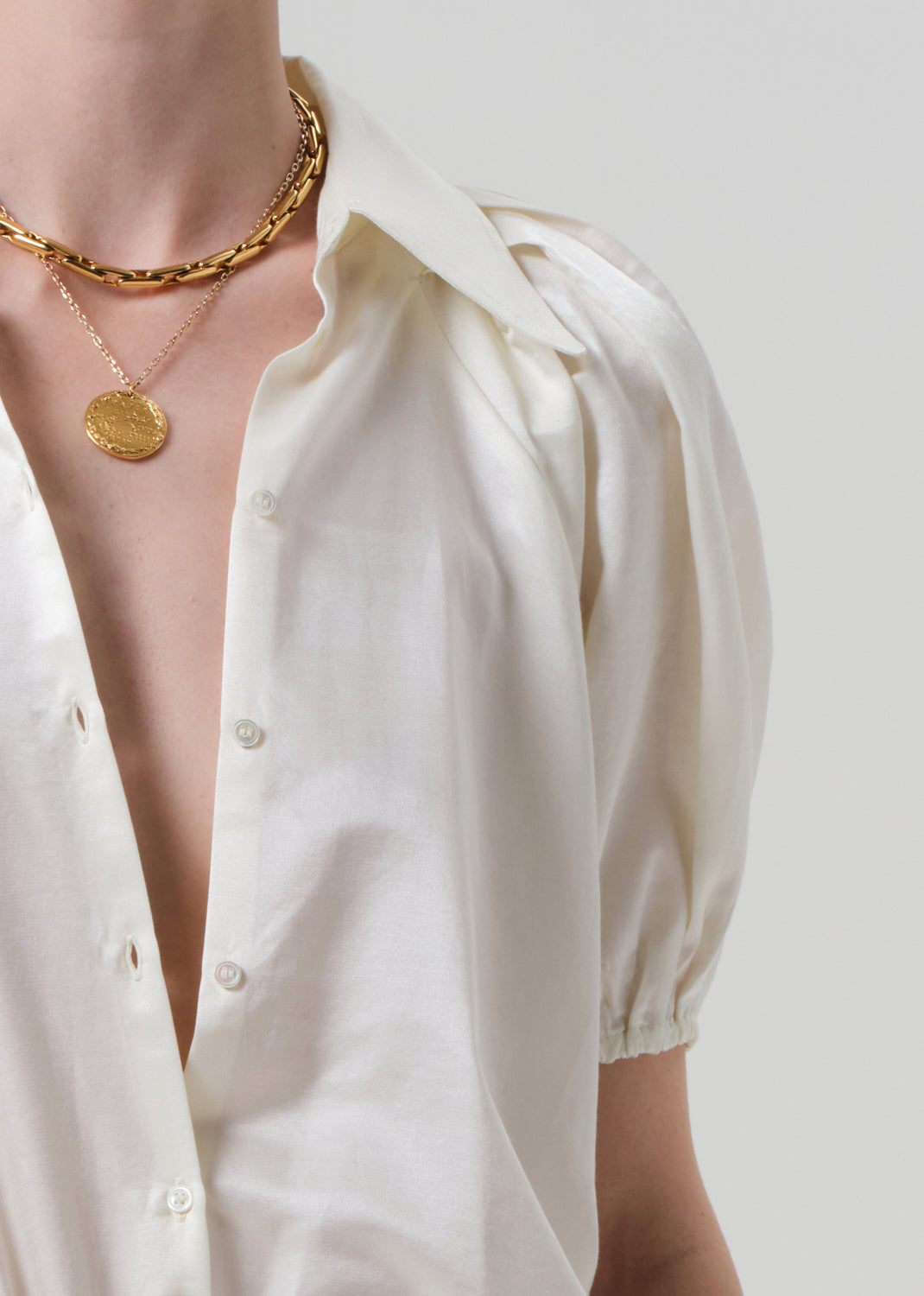 Person wearing a white shirt with a gold necklace on a plain background