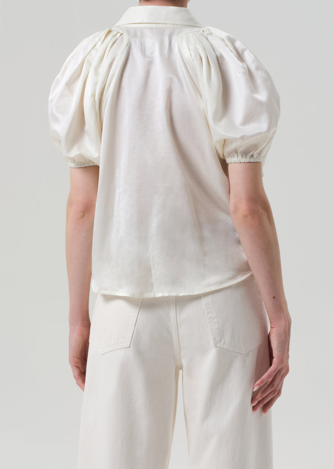 Person wearing a white blouse with puff sleeves and white pants on a light gray background