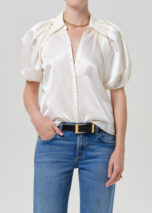 Woman wearing a white puff sleeve button-up blouse with medium blue straight leg jeans on a grey background.